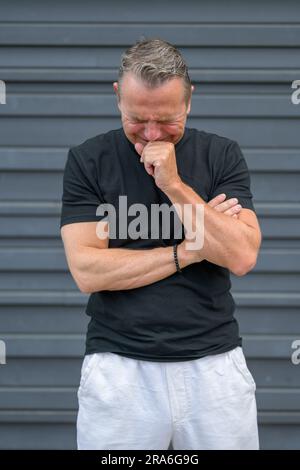 Dreiviertel langes Porträt eines notleidenden älteren Mannes mit einer Hand am Kinn vor einer blauen Wand Stockfoto