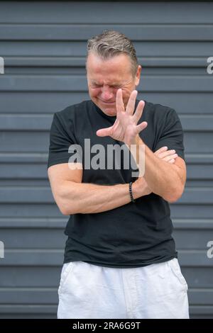 Ein dreiviertel langes Porträt eines notleidenden älteren Mannes mit einer Hand vor der Kamera, die vor einer blauen Wand „STOPP“ sagt Stockfoto