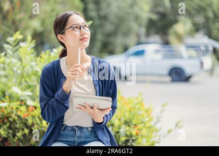 Asiatisches Teenager-Mädchen der Universität, das Tablet-Denken verwendet, löst Probleme beim Lernen Bildung Menschen Lebensstil auf dem Schulgelände. Stockfoto