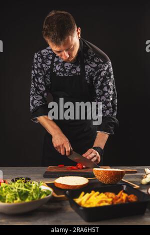 Der Koch schneidet Tomaten für Burger. Die Zubereitung eines Burgers. Stockfoto