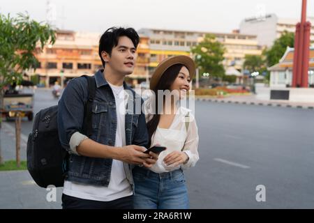 Glückliches Lächeln Junges asiatisches Paar Touristen, die auf der Straße in Bangkok in Thailand ein Taxi rufen, ohne Telefon oder Technologie zu benutzen Stockfoto