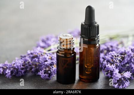 Zwei dunkle Flaschen ätherisches Aromatherapie-Öl mit frischen Lavendelblumen auf einem Tisch, mit Kopierraum Stockfoto