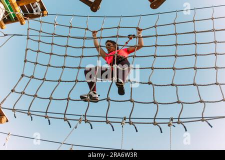 Junge Kletterer, die Schwierigkeiten haben, im Abenteuerpark an der Seile zu hängen Stockfoto