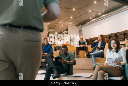 Gruppe von generationenübergreifenden, multiethnischen Menschen, die eine Pause von der Präsentation bei der Arbeit machen. Sie unterhalten sich unterhaltsam und lächeln Stockfoto