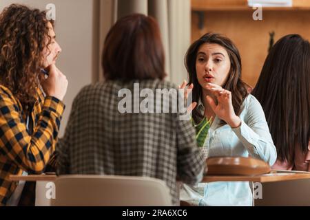 Drei junge und attraktive Arbeitsfreunde sitzen zusammen und unterhalten sich in der Bürokantine Stockfoto