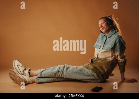 Süßes Ingwermädchen, das sich entspannt, während es auf dem Boden des Fotostudios sitzt Stockfoto