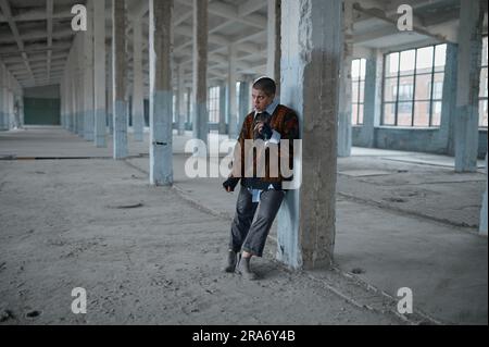 Obdachlose Punk-Frau, die kaum auf den Füßen stand, lehnte sich an die Säule Stockfoto