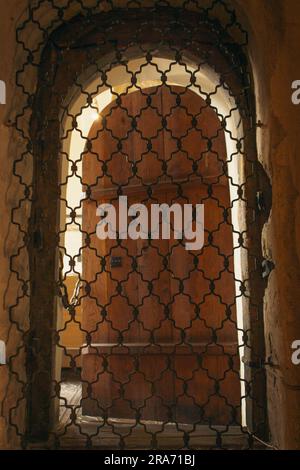 Antikes Portal in der Kirche. Eingang mit Eisengitter im Schloss. Alte Holztür mit Gitterrosten. Zelle im mittelalterlichen Tempel. Ein alter Architekturbogen. Stockfoto