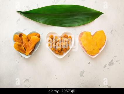 Getrocknete Mangoscheiben und -Kugeln in herzförmigen Platten auf hellem Hintergrund. Stockfoto