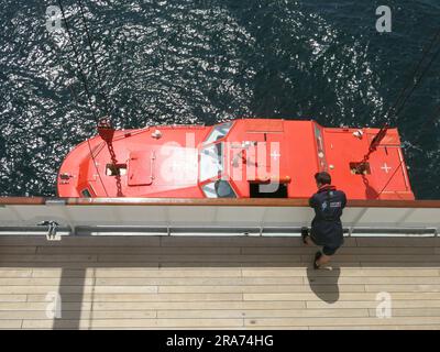 Ein Besatzungsmitglied des Kreuzfahrtschiffs „Heritage Adventurer“ beobachtet vom Deck aus, wie einer der Beißer für einen Passagiertransfer ins Wasser abgesenkt wird. Stockfoto