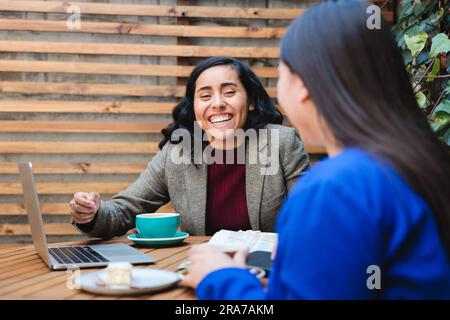 Finanzsicherheits-Gespräch: Junge Latina, die eine Lebensversicherung an eine andere Frau in einem gemütlichen Café verkauft Stockfoto