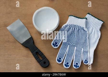 Baugruppensatz, Bauspachtel, Dose mit weißem Kitt, Schutzhandschuhe, auf Sperrholzoberfläche. Stillleben. Einbausatz für Kitt. Flach liegend, Draufsicht Stockfoto