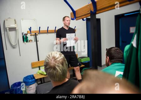 PRODUKTION – 01. Juli 2023, Niedersachsen, Deblinghausen: Tim Steinmetzger, Trainer und Spieler der zweiten Mannschaft von tun Steyerberg, steht vor seinen Spielern in der Umkleidekabine der örtlichen Turnhalle vor dem Beginn des Spiels gegen SV Rot Weiß Deblinghausen und erläutert die Aufstellung. Saßnick, 28, tritt seit 17 Jahren an der TuS Steyerberg im Bezirk Nienburg/Weser. Sie ist derzeit Stürmer für die dritte Mannschaft in der dritten Distriktabteilung. Manchmal hilft sie auch im zweiten Team einer der obigen Abteilungen. Aber das ist für sie erst seit De möglich Stockfoto