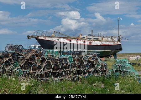 Altes Fischerboot am Ufer, umgeben von Hummertöpfen Stockfoto