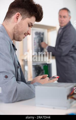 Der Vorgesetzte erkennt einen Auszubildenden am Arbeitsplatz mit seinem Smartphone Stockfoto