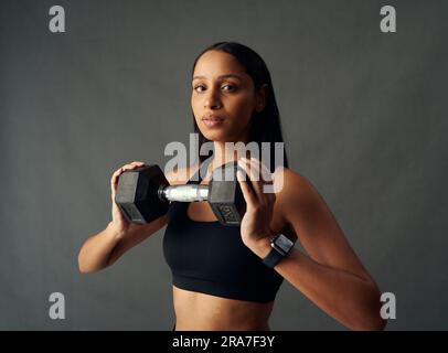 Porträt einer jungen Biracial-Frau im Sport-BH mit Hantel im Studio Stockfoto