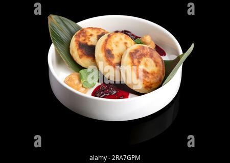 Nahaufnahme von Hüttenkäse-Pfannkuchen mit Sauerrahm und Marmelade auf schwarzem Hintergrund mit Reflexion. Speiserestaurant Stockfoto