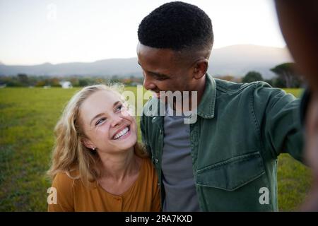 Glückliches, junges, multiethnisches Paar in legerer Kleidung, das sich auf dem Feld anschaut Stockfoto