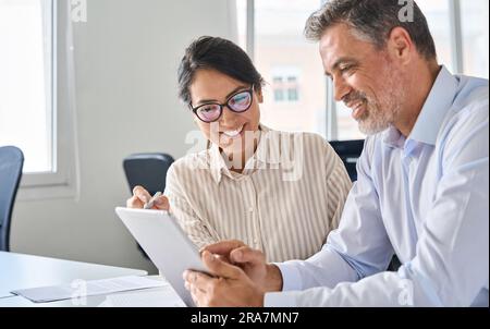 Zwei zufriedene Geschäftsleute, die im Büro ein digitales Tablet verwenden. Stockfoto