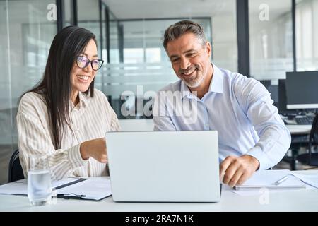 Zwei zufriedene und vielseitige professionelle Kollegen, die im Büro mit einem Laptop arbeiten. Stockfoto