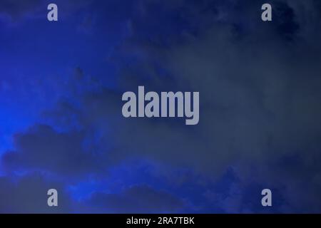 Die Wolken bewegen sich schnell über den dunklen Nachthimmel, die Lichtblitze des sich nähernden Sturms erhellen sie. Stockfoto
