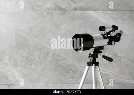 Stativ mit modernem Teleskop nahe der grauen Wand, Nahaufnahme. Platz für Text Stockfoto