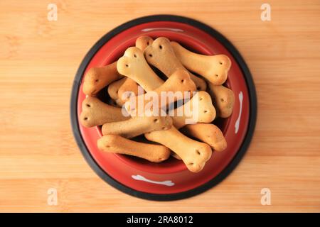 Knochenförmige Hundekekse in der Fütterschüssel auf dem Holztisch, Draufsicht Stockfoto