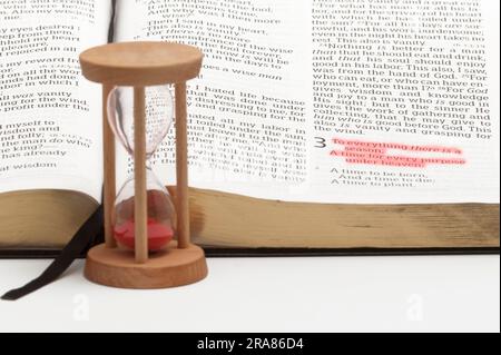 Sanduhr und offene bibel über das Buch des Kirchenlehrers mit selektivem Fokus auf Vers 1 von Kapitel 3, rot hervorgehoben. Isoliert auf weißem Hintergrund. Stockfoto