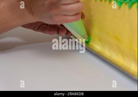 Eine Frau, die einen grünen und gelben Geburtstagskuchen mit einer Nahaufnahme der Konditortüte dekoriert. Stockfoto