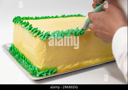 Eine Frau, die einen grünen und gelben Geburtstagskuchen mit einer Nahaufnahme der Konditortüte dekoriert. Stockfoto