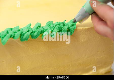 Eine Frau, die einen grünen und gelben Geburtstagskuchen mit einer Nahaufnahme der Konditortüte dekoriert. Stockfoto