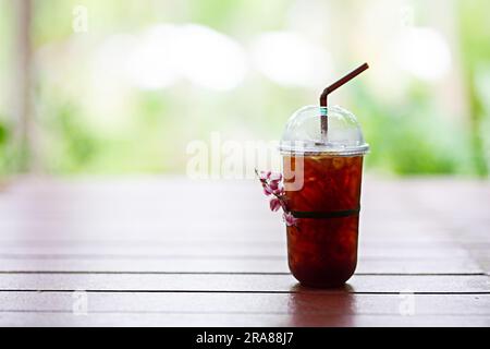 Plastikkaffeetasse, gefrorener Americano (schwarzer Kaffee) auf einem Holztisch im Garten Stockfoto