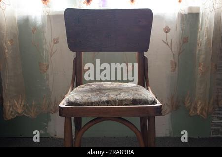Der alte braune Stuhl steht im Schlafzimmer in der Nähe des Fensters aus der Nähe Stockfoto