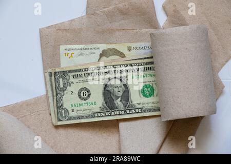 Ein amerikanischer Dollar und einhundert ukrainische Hrywna liegen auf Toilettenpapier auf einer Nahaufnahme mit weißem Hintergrund Stockfoto