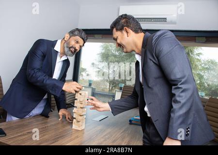 Zwei glückliche, junge indische Geschäftsleute, die einen Anzug tragen und Holzblöcke zusammenlegen, Wachstumsplan und Erfolg, Immobilien und Real Stockfoto