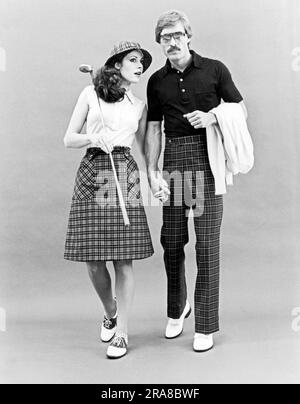 Vereinigte Staaten: c. 1962 Ein stilvolles Paar in karierter Golfkleidung, das Hände hält. Sie trägt Sattelschuhe und er hat weiße tasselierte Slipper. Stockfoto