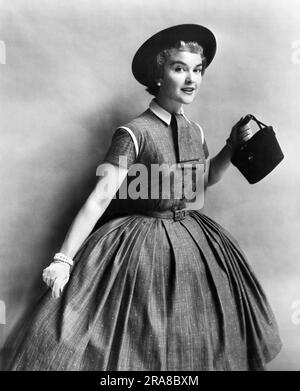 Vereinigte Staaten: c. 1954 Eine modische junge Frau, die ein gewebtes Baumwollkleid von Kay Junior mit einem Flair für „Young in Heart“ vorführt. Stockfoto