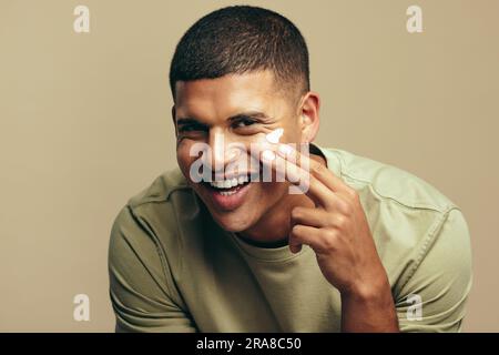 Portrait eines glücklichen jungen Mannes, der ein Schönheitsprodukt auf sein Gesicht aufträgt und sein frisches und gesundes Aussehen behält. Ein hübscher junger Mann, der seinen Hautgeist verwöhnt Stockfoto