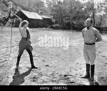 Hollywood, Kalifornien: 16. März 1925 Schauspielerin Anna Q. Nilsson bereitet sich darauf vor, eine Zigarette aus dem Mund des australischen Star-Athleten Snowy Baker mit einer Peitsche zu schlagen. Baker hat ihr den Stunt beigebracht und sie soll die einzige Frau in Amerika sein, die das kann. Stockfoto