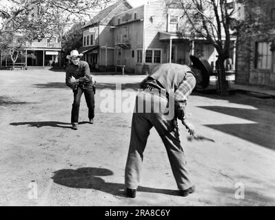 Hollywood, Kalifornien: c. 1950 der gute Cowboy (weißer Hut) zieht den bösen Cowboy (schwarzer Hut) an und schießt ihm in dieser Western-Filmszene die Waffe aus der Hand. Stockfoto