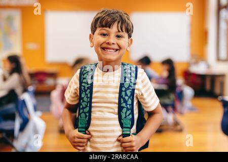 Lebensstil des Lernens: Grundschulkinder, die sich auf den ersten Schultag freuen. Ein kleiner Junge, der in der Kamera lächelt, während er in einer Grundschule C steht Stockfoto