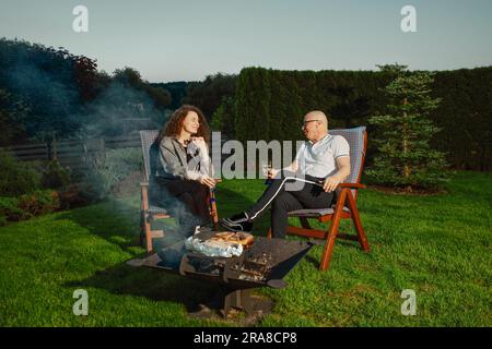 Glückliches Paar beim Grillen im Freien. Mann dreht Würstchen auf dem Grill. Stockfoto
