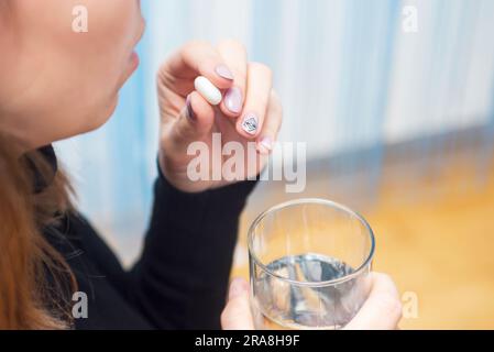 Weibliche Hände halten eine Tablette und ein Glas Wasser nah heran Stockfoto