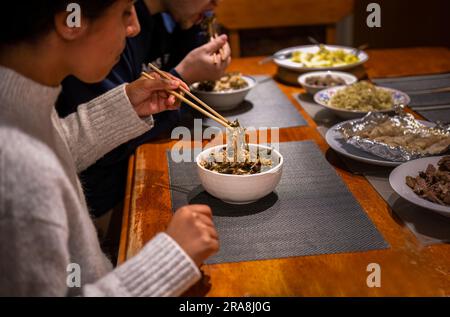 Ein Paar hält Stäbchen und isst zu Abend. Gemüse- und Rindfleischgerichte auf dem Esstisch. Hausmannskost- und Essenskonzept. Stockfoto