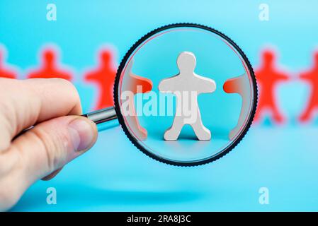 Eine männerhand mit einer Lupe zielt auf eine Reihe von hölzernen Figuren von Menschen Stockfoto