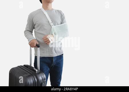 Reiseversicherungskonzepte. Ein junger Mann mit einer Handverletzung, der eine Schiene trägt, einen gebrochenen Arm hat, schwarzes Gepäck in der Hand hält, isoliert auf weißem Hintergrund Stockfoto