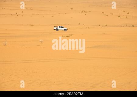 Ein SUV, der die Wüste mit gelbem Sand an einem heißen Tag durchquert Stockfoto