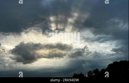 Die Sonne scheint durch dunkle Wolken, farbenfroher dramatischer Himmel mit Wolken bei Sonnenuntergang. Naturwolkenlandschaft im Hintergrund Stockfoto
