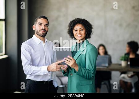 Zwei Glückliche Hispanische Kollegen, Die Im Büro Mit Einem Digitalen Tablet Posieren Stockfoto