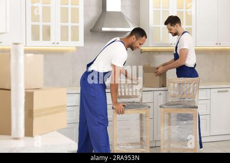 Männliche Umzugsleute mit Stühlen im neuen Haus Stockfoto